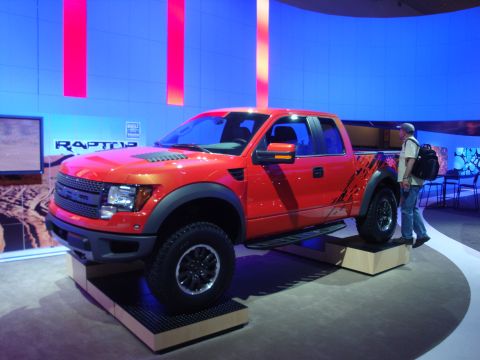 1993 Ford Taurus - A red Ford F-150 SVT Raptor pickup truck is displayed at an auto show with a person standing nearby.