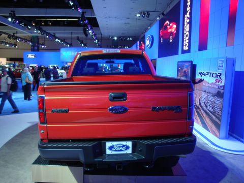 1993 Ford Taurus - Orange Ford F-150 Raptor SVT pickup truck displayed at an auto show with "Ford" branding visible.