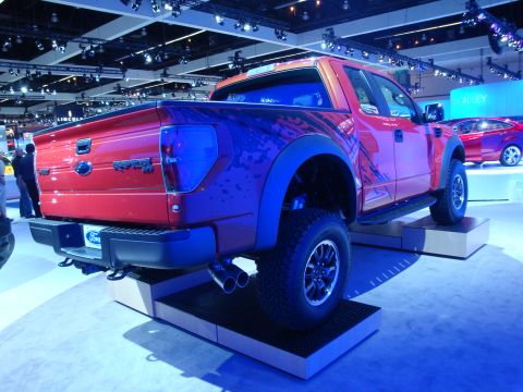 1993 Ford Taurus - This Ford Raptor pickup truck is displayed at an auto show with a red car in the background.