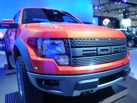 1993 Ford Taurus - Front view of an orange Ford F-150 Raptor at an auto show, with 'FORD' clearly visible on the grille.