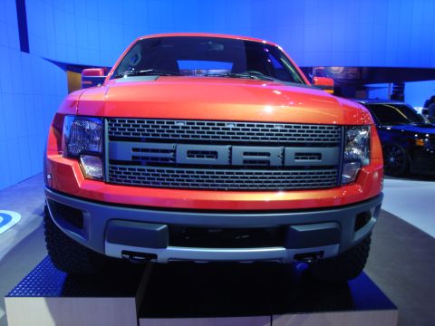1993 Ford Taurus - This orange Ford F-150 SVT Raptor is displayed at an auto show with a blue backdrop.