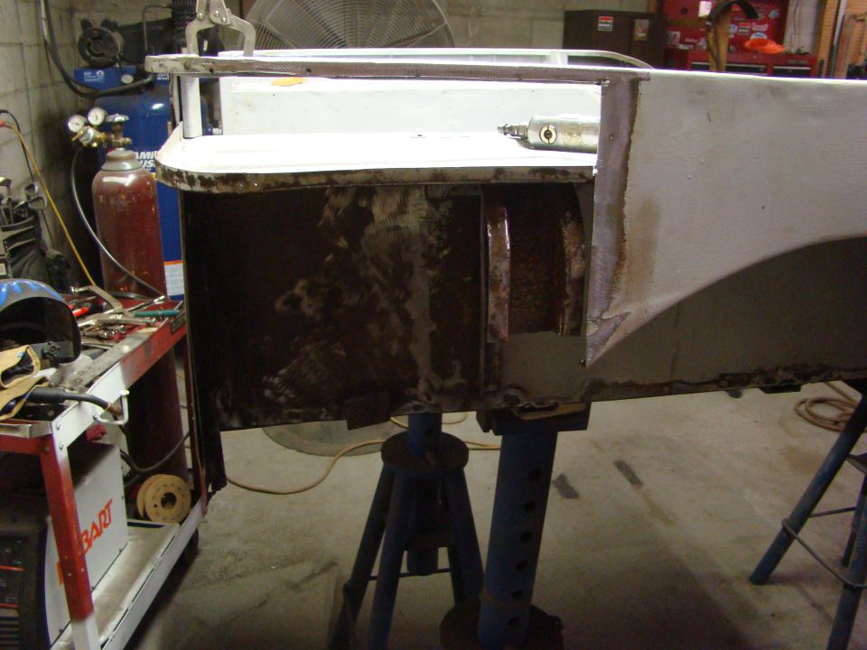 close-up of rusted and welded vehicle body panel on stands, with tools and equipment in background