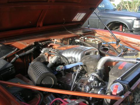 1972 Ford Bronco - Engine bay of an orange vehicle with chrome accents and an aftermarket air filter, with another vehicle in the background.