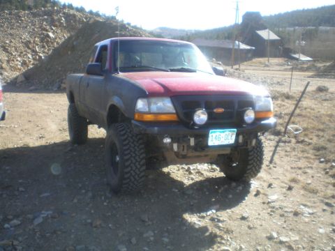 1996 Ford Bronco - A modified Ford Ranger pickup truck sits parked on a dirt road in a mountainous area.
