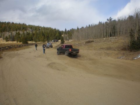 1996 Ford Bronco - A group of trucks navigate a dusty trail through a wooded, hilly landscape under a cloudy sky.