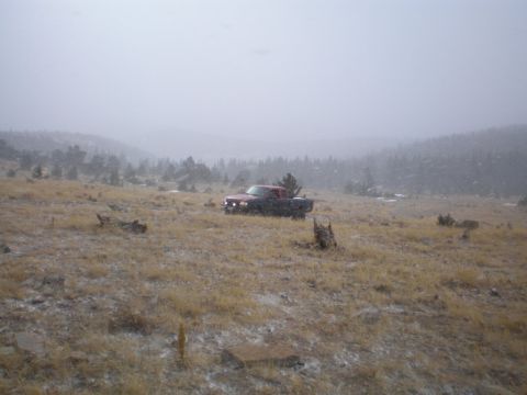 1996 Ford Bronco - A red pickup truck is parked in a field during a snowfall, with hills and trees visible in the distance.