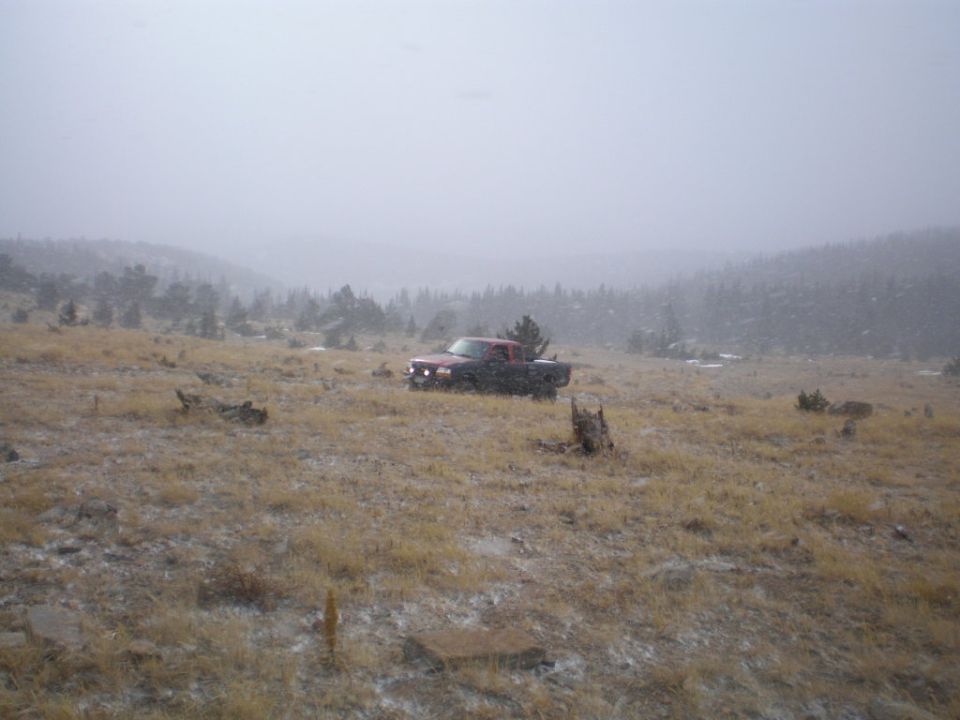Red pickup truck in a snowy field with trees and hills in background