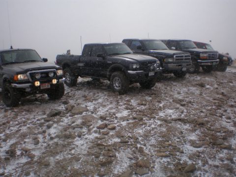 1996 Ford Bronco - A group of pickup trucks are parked on a rocky, snow-dusted terrain under an overcast sky.