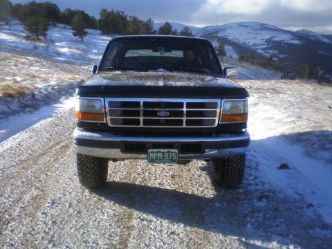 1996 Ford Bronco - A black Ford Bronco is parked on a snowy road with mountains in the background.
