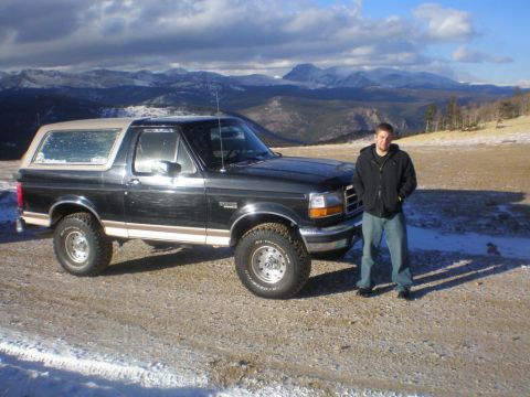 1996 Ford Bronco - A man poses with his black 1996 Ford Bronco, a tan removable top, against a backdrop of snow-dusted mountains.