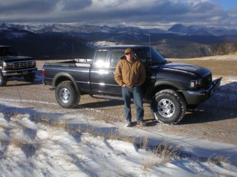 1996 Ford Bronco - Man and two pickup trucks in a snowy mountain landscape with cloudy skies.