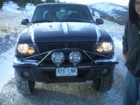 1996 Ford Bronco - A dark colored Ford Ranger is parked on a snowy road with a person standing to the right.