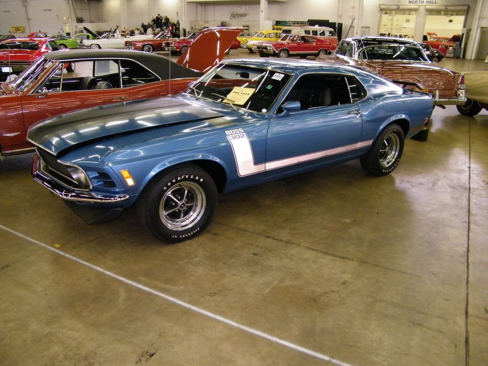 Blue Ford Mustang fastback with BOSS 302 stripes at an indoor car show, front three-quarter view