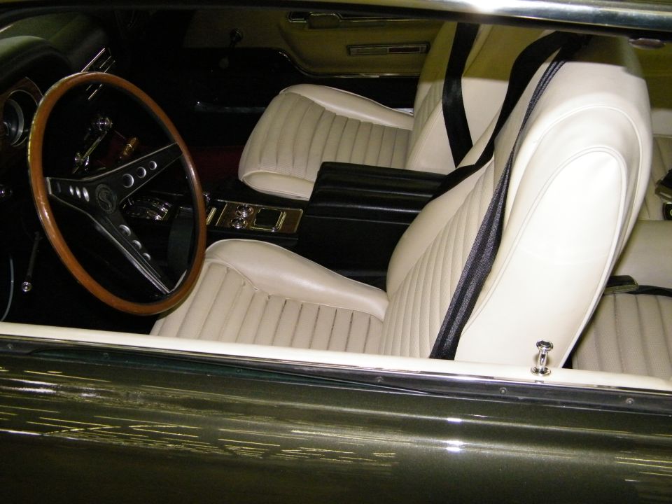 White bucket seat interior and wood steering wheel with Cobra emblem in a dark green 1968 Mustang