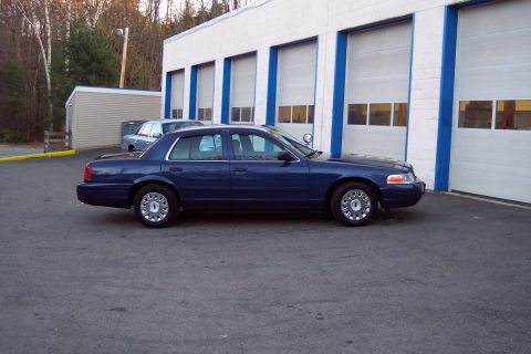 2001 Ford Crown Victoria - A dark blue 2001 Ford Crown Victoria is seen parked outside a commercial building with multiple garage bays.