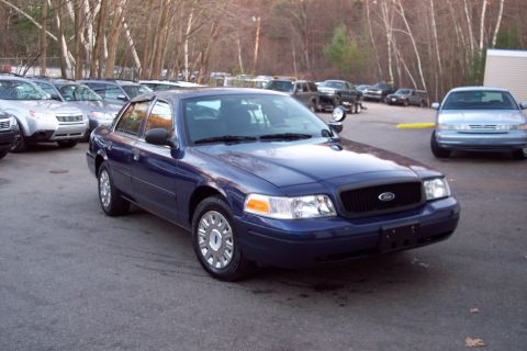 2001 Ford Crown Victoria - Blue Ford Crown Victoria police car parked in a lot with other vehicles visible.