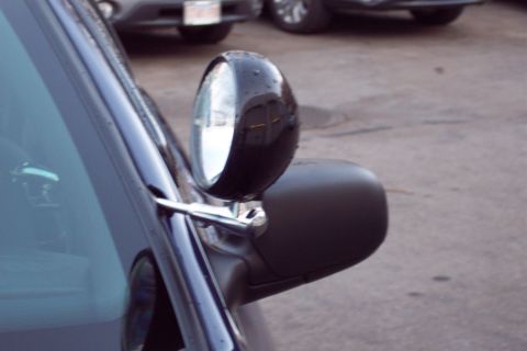2001 Ford Crown Victoria - Close-up view of a side mirror on a dark-colored vehicle, with another car visible in the background.