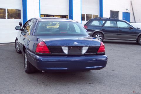 2001 Ford Crown Victoria - A blue 2001 Ford Crown Victoria is parked in front of a garage with another vehicle behind it.