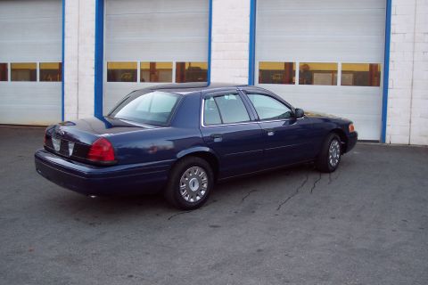 2001 Ford Crown Victoria - A dark blue 2001 Ford Crown Victoria is seen from a three-quarter front angle in front of a building with garage doors.