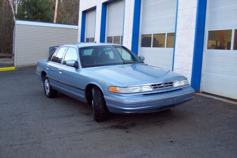 2001 Ford Crown Victoria - A light blue sedan is parked in front of a building with multiple garage doors.