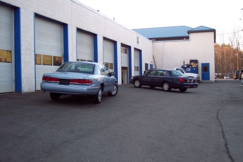 2001 Ford Crown Victoria - Two Ford Crown Victorias are parked in front of a commercial building with multiple garage bays.