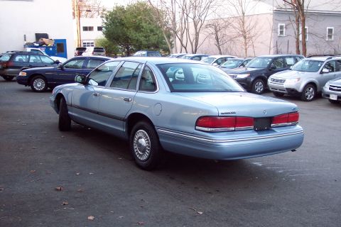 2001 Ford Crown Victoria - A light blue 2001 Ford Crown Victoria sedan is parked in a lot with other vehicles.