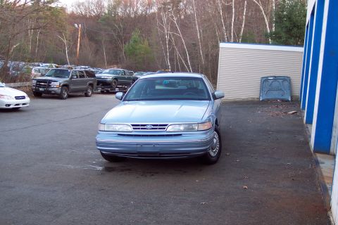 2001 Ford Crown Victoria - A light blue 2001 Ford Crown Victoria is parked in front of a building, with other vehicles visible in the background.
