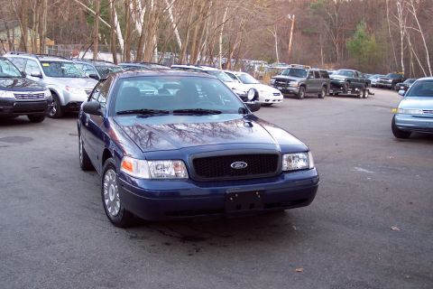 2001 Ford Crown Victoria - A blue 2001 Ford Crown Victoria police car is parked in a lot with several other vehicles visible.