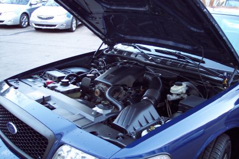 2001 Ford Crown Victoria - The engine bay of a blue Ford Crown Victoria is shown with the hood up, parked next to two other vehicles.