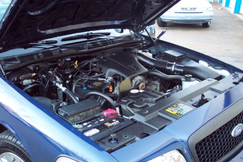 2001 Ford Crown Victoria - The engine bay of a blue car is shown with the hood open. Another vehicle is visible in the background.