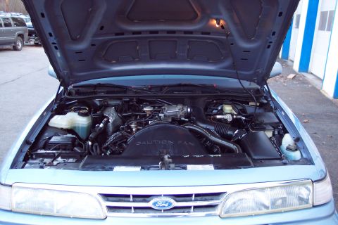 2001 Ford Crown Victoria - The engine bay of a 2001 Ford Crown Victoria is open for viewing, with a nearby SUV visible in the background.