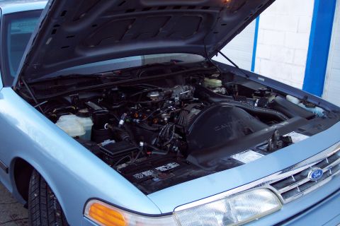 2001 Ford Crown Victoria - The engine bay of a light blue 2001 Ford Crown Victoria is visible with the hood raised, revealing the engine and surrounding components.