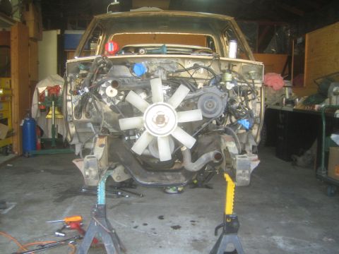 1990 Ford Bronco - Head-on view of a gutted pickup truck front end on jack stands, showing the white cooling fan and bare frame.