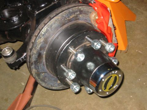 1995 Ford Bronco - Close-up of a vehicle's front wheel hub assembly, a chrome hubcap with a yellow emblem.