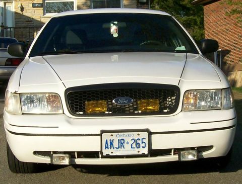 2003 Ford Crown Victoria - Frontal view of a white 2003 Ford Crown Victoria, showing its grille and headlights.