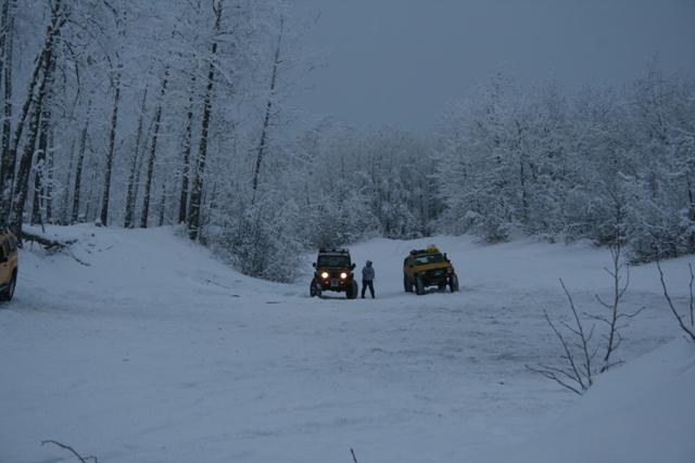 Two off-road vehicles parked in a snow-covered forest clearing with trees in the background