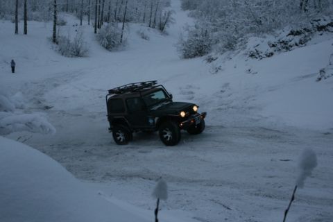1990 Chevrolet Suburban - Jeep Wrangler navigates a snow-covered path with trees in the background.