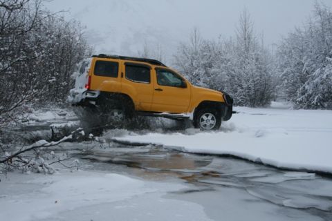 1990 Chevrolet Suburban - A yellow SUV navigates through a partially frozen body of water during a snowy day.