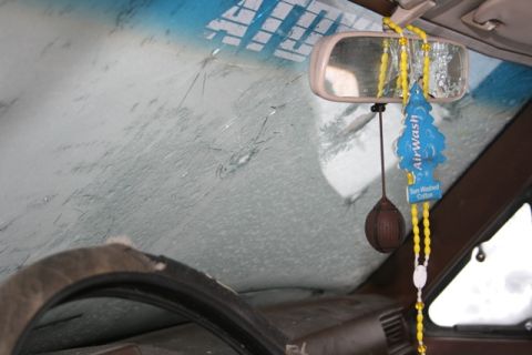 1990 Chevrolet Suburban - The interior of a vehicle shows a cracked windshield, a rearview mirror, and an AirWash air freshener hanging from the mirror.