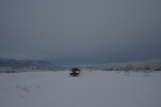 Yellow SUV driving through snow with headlights on