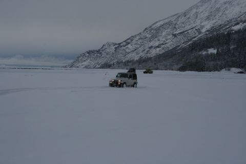 1990 Chevrolet Suburban - Multiple vehicles traverse a snowy landscape with a mountain range in the background.