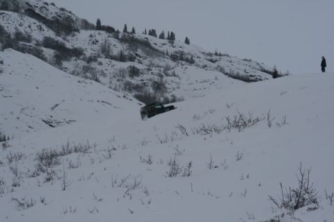 1990 Chevrolet Suburban - A dark SUV navigates a snow-covered terrain, with a lone figure observing from a distant ridge.