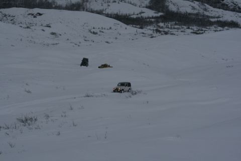 1990 Chevrolet Suburban - A Jeep Wrangler navigates a snow-covered landscape with sparse vegetation and distant hills.