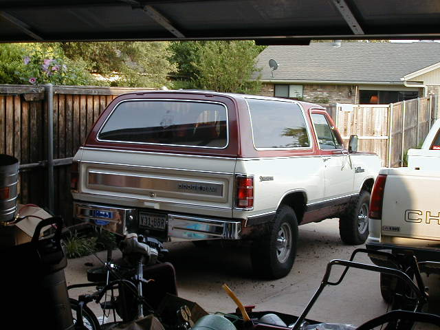 Two-tone white and maroon Dodge Ramcharger SUV in a driveway, rear three-quarter view from a garage