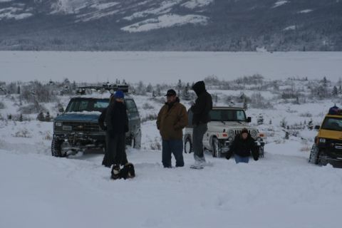1990 Chevrolet Suburban - People and their vehicles are stranded in a snowy landscape with a frozen lake in the background.