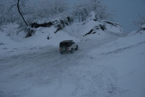 1990 Chevrolet Suburban - Jeep Wrangler navigates a snowy path with trees and snow-covered hills in the background.