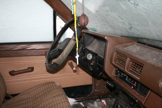 Brown interior with plaid seat, cracked windshield, and rosary hanging from rearview mirror