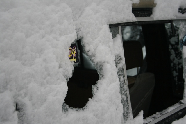 Snow covers a vehicle's side window, revealing a license plate with '04' visible