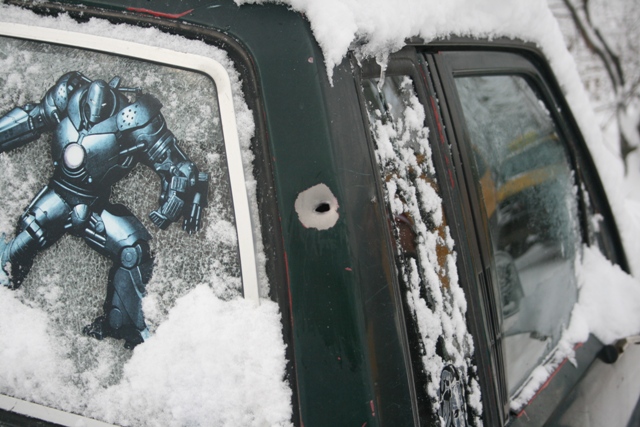 Rear window with Iron Man sticker and bullet hole, covered in snow