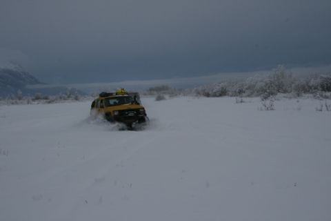 1990 Chevrolet Suburban - A yellow Jeep Cherokee XJ navigates a snowy landscape, kicking up snow as it drives.